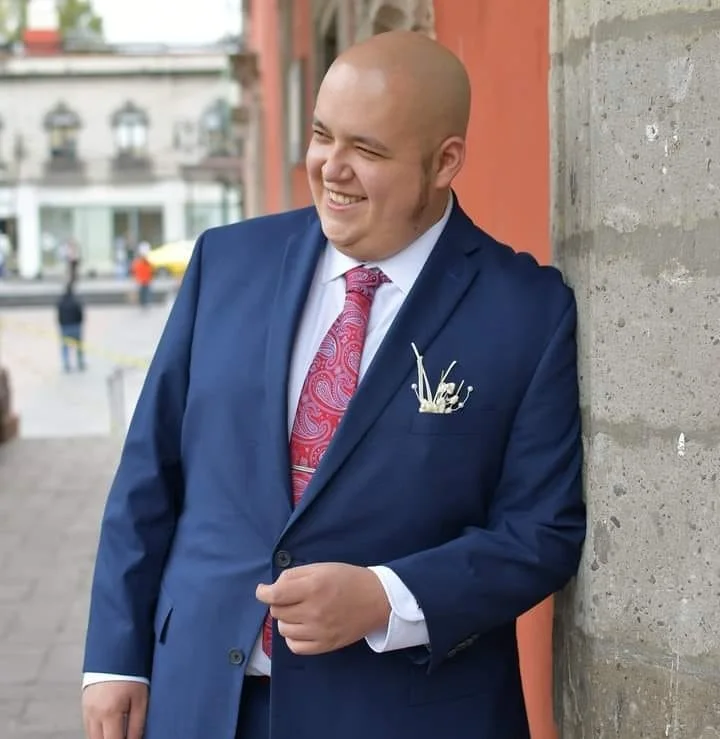 Raúl Alcocer in a blue suit, smiling